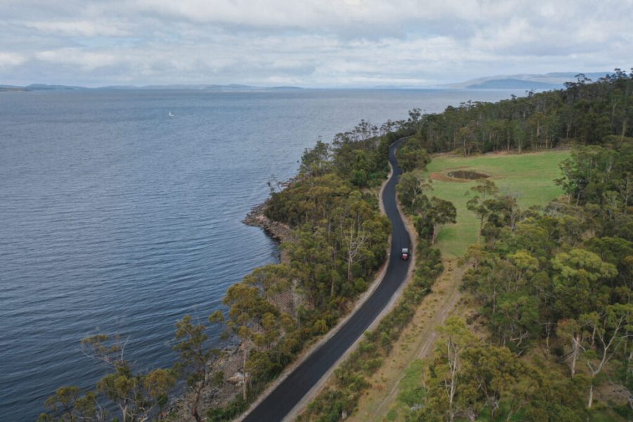 Aerial image of windy road through bushland alongside ocean.