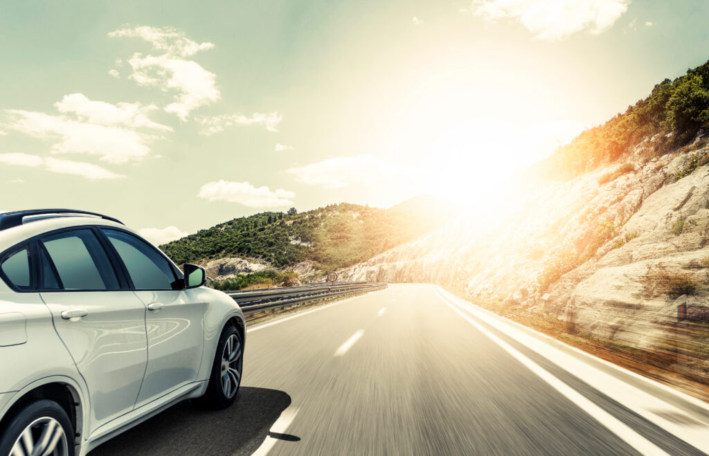 Image of white car driving along road with sun reflecting.