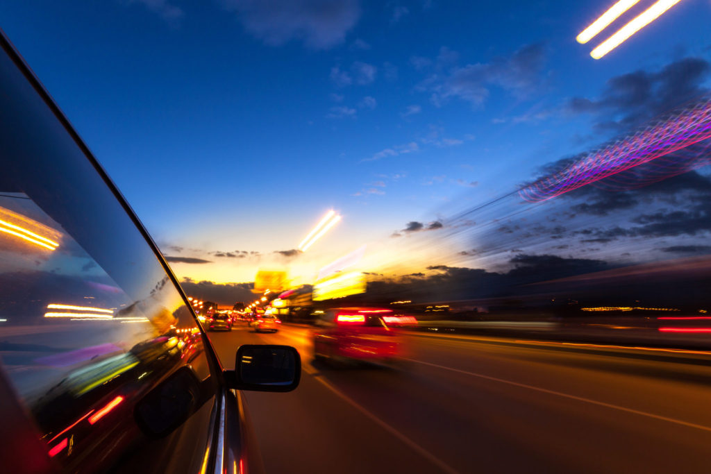 Close up of cars driving along road at dust, moving cars are blurred.