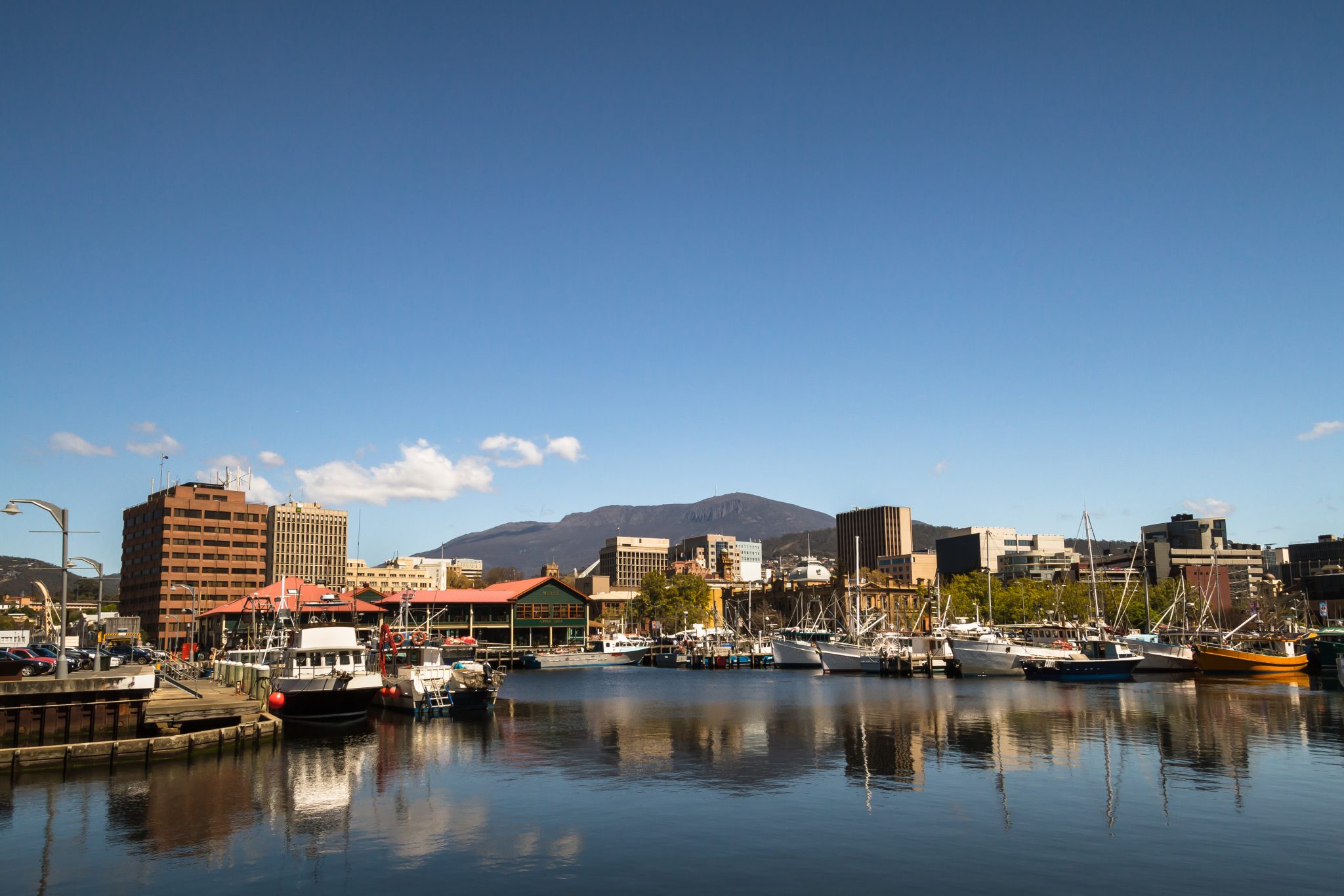 Hobart waterfront showing water in foreground, buildings and boats in midground, and kunanyi Mount Wellington in background.