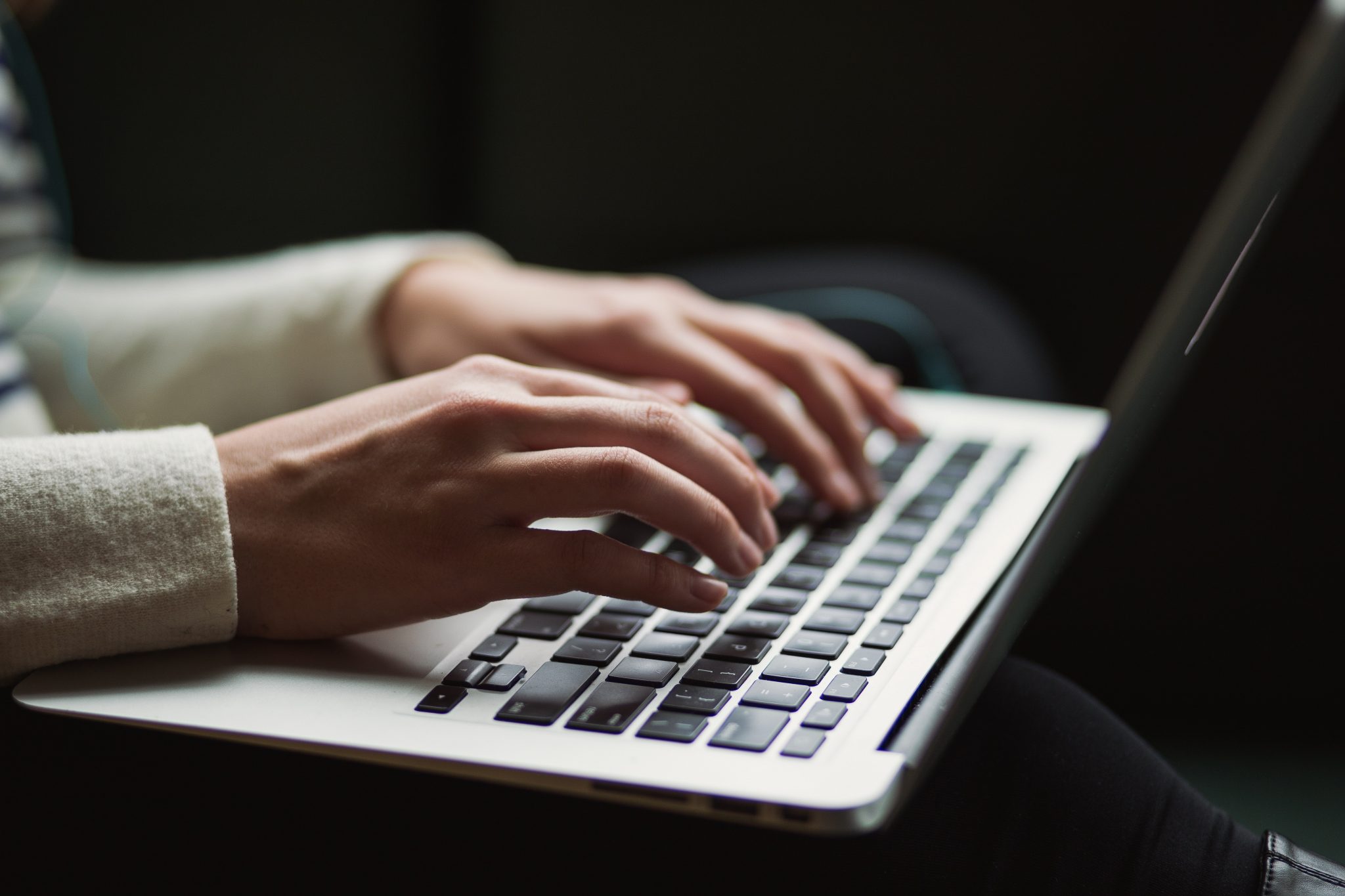 Close up of hands typing on laptop, dark background.