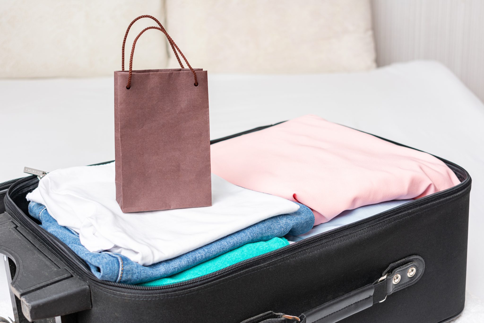 Small brown gift bag sitting on top of open suitcase with folded clothes.