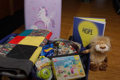 An open child's suitcase packed with books, toys, blanket and clothing.