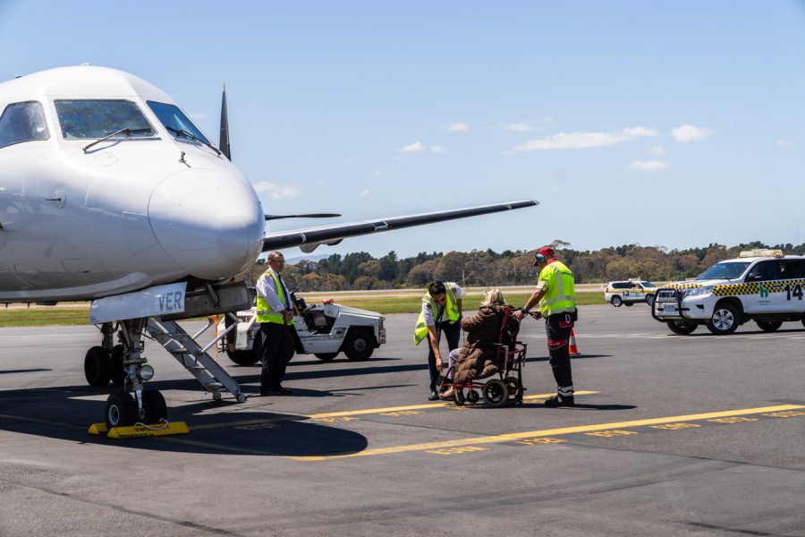A lady on a wheelchair being assisted by the ground staff to board an aircraft.