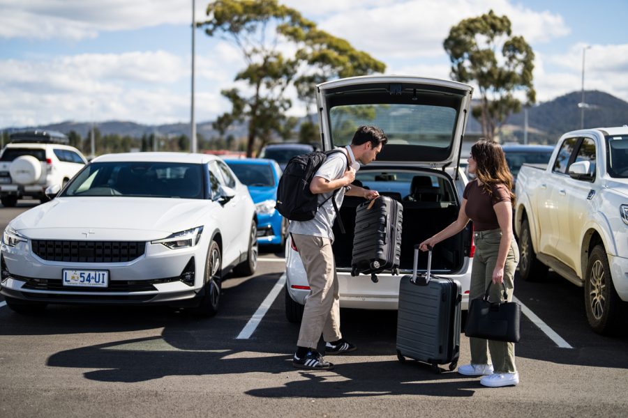Man and woman taking luggage out of boot of car in car park.
