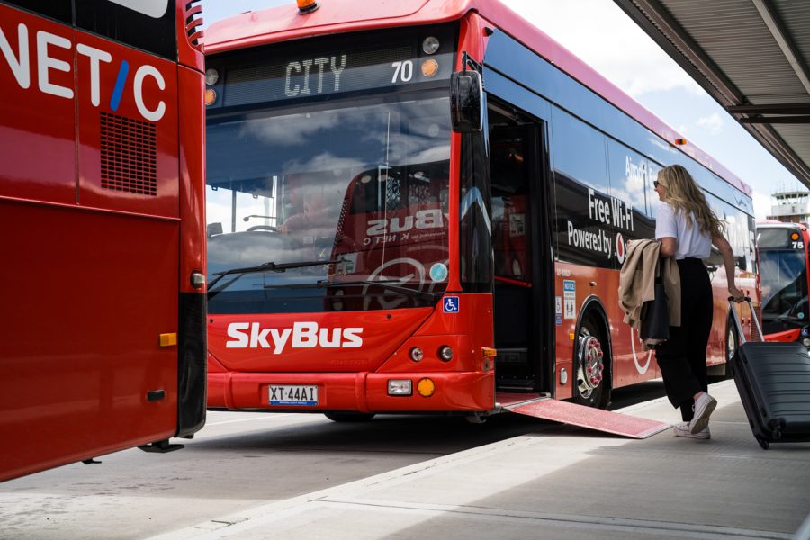 A woman about to board a Skybus, showing City on its destination display.