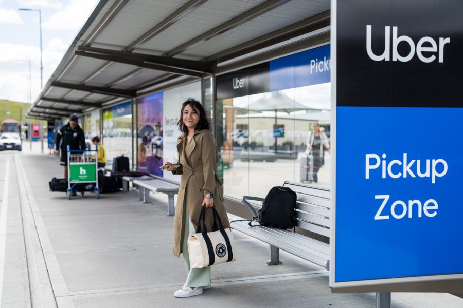 Smiling woman holding a phone and bag in Uber shelter at airport.