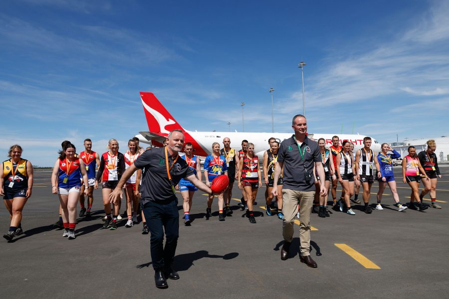 A group of people walking on an airport tarmac with a Qantas airplane in the background.