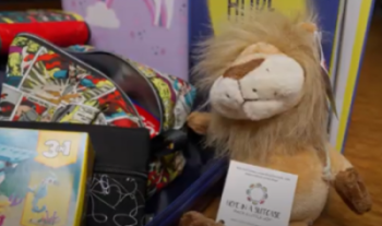 A collection of children's items including a colorful comic-themed backpack, a plush lion toy with a 'Hope in a Suitcase' tag, and a puzzle box featuring animal illustrations.