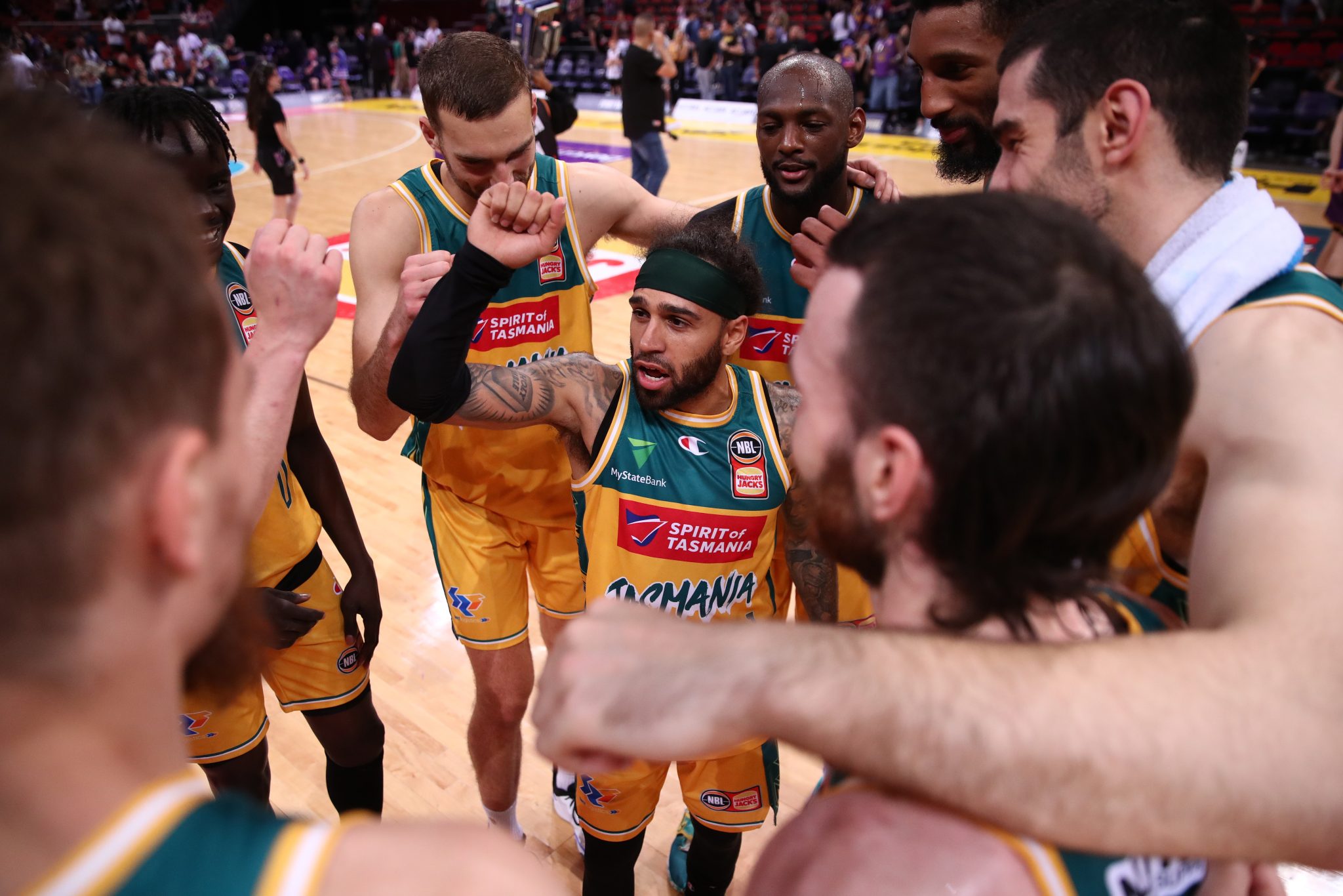 Tasmania Jack Jumpers players in a team discussion circling around a player in the middle.