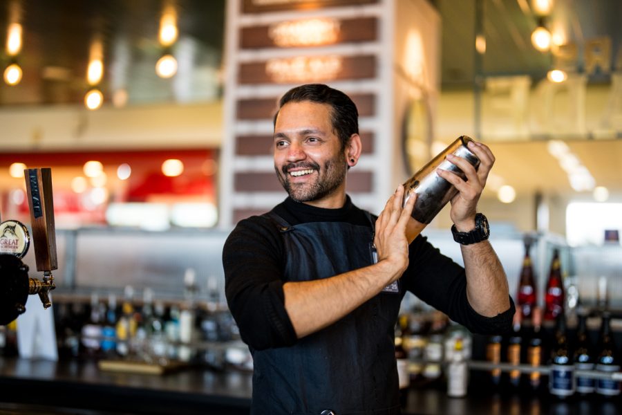 Smiling man shaking a cocktail in a bar setting.