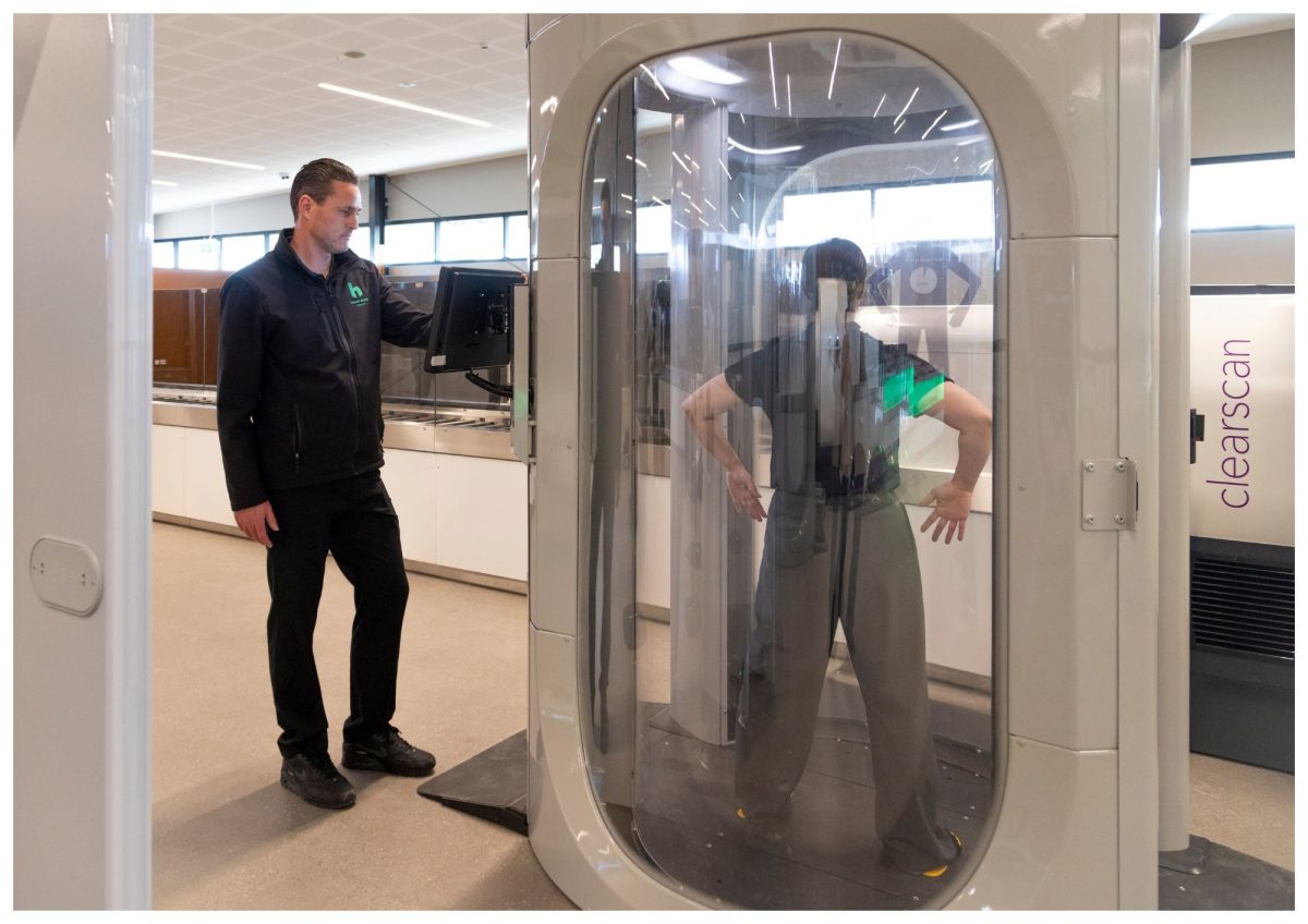 A lady inside a full-body scanner with hands raised, while a security officer monitors the process nearby.